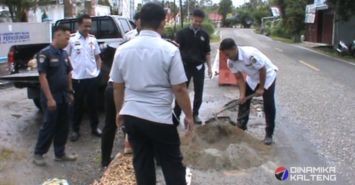 Proses perbaikan jalan berlubang sedang berlangsung, di mana salah satu petugas dengan cermat menutupi lubang menggunakan campuran material sambil diawasi oleh rekan-rekannya. (foto: DINAMIKA KALTENG/mas)
